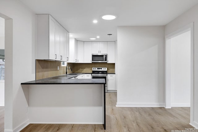 kitchen featuring kitchen peninsula, white cabinets, decorative backsplash, and appliances with stainless steel finishes