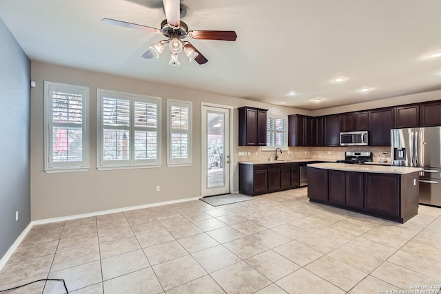 kitchen featuring tasteful backsplash, a center island, dark brown cabinets, light tile patterned floors, and appliances with stainless steel finishes