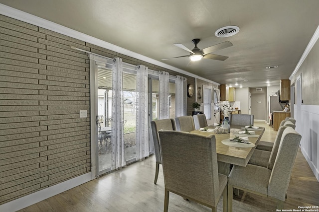 dining space with ceiling fan, brick wall, crown molding, and hardwood / wood-style floors