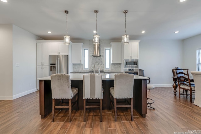 kitchen featuring white cabinets, a kitchen island with sink, pendant lighting, and appliances with stainless steel finishes