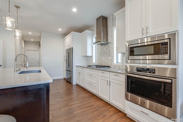 kitchen featuring appliances with stainless steel finishes, white cabinets, sink, pendant lighting, and wall chimney exhaust hood