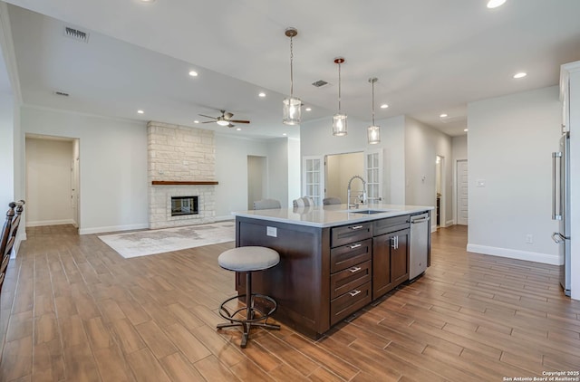 kitchen with hanging light fixtures, sink, a fireplace, a kitchen island with sink, and dark brown cabinetry