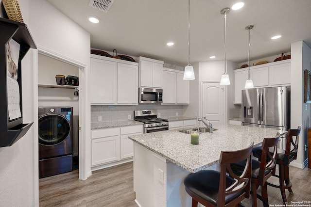 kitchen featuring white cabinets, washer / dryer, decorative light fixtures, stainless steel appliances, and sink