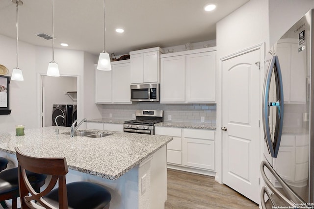 kitchen with appliances with stainless steel finishes, white cabinetry, sink, pendant lighting, and a center island with sink