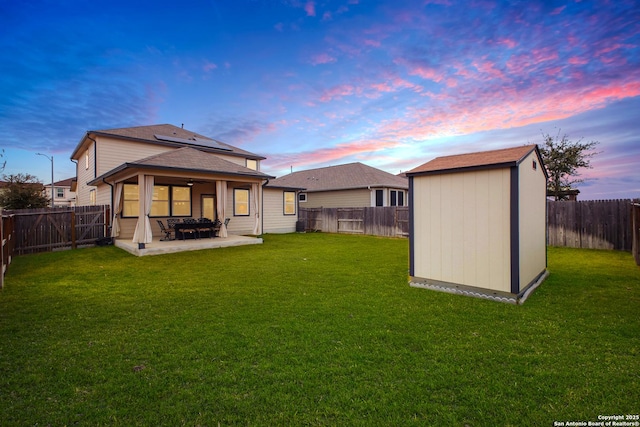 back house at dusk with a storage shed, a yard, and a patio