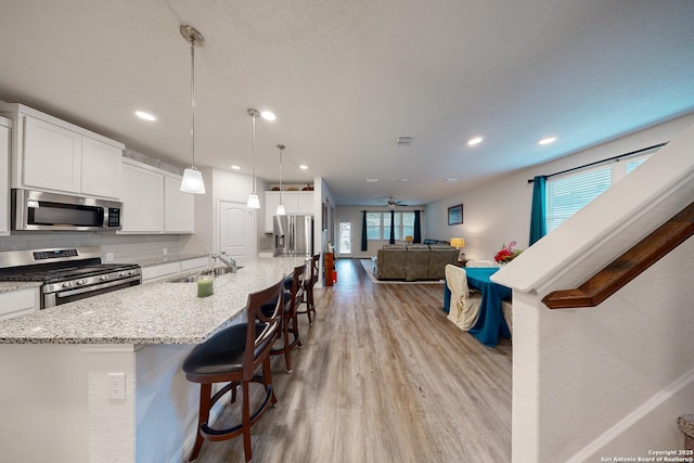 kitchen featuring decorative light fixtures, backsplash, white cabinets, a breakfast bar, and stainless steel appliances