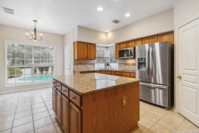 kitchen with hanging light fixtures, backsplash, light stone counters, a kitchen island, and stainless steel appliances