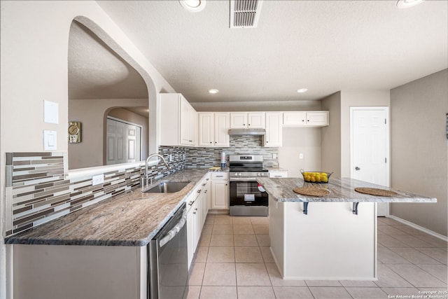 kitchen with a center island, white cabinetry, stainless steel appliances, stone countertops, and light tile patterned flooring