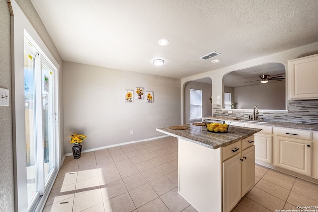 kitchen with sink, light tile patterned floors, a healthy amount of sunlight, a center island, and decorative backsplash