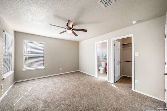 unfurnished bedroom with carpet, ensuite bath, a walk in closet, a closet, and ceiling fan