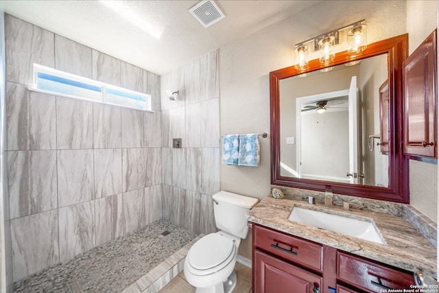 bathroom with a tile shower, toilet, and vanity