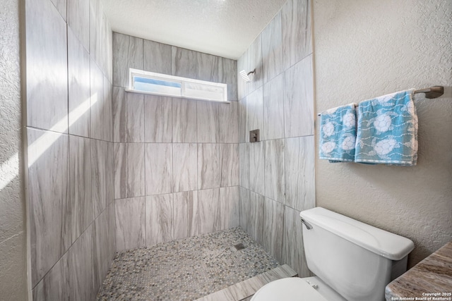 bathroom featuring a textured ceiling, tiled shower, and toilet