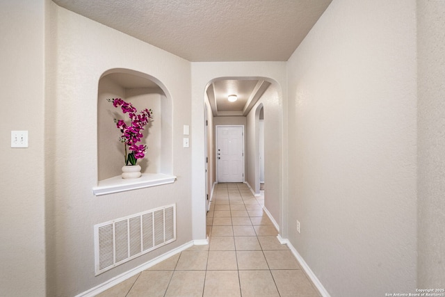 hall featuring a textured ceiling and light tile patterned floors