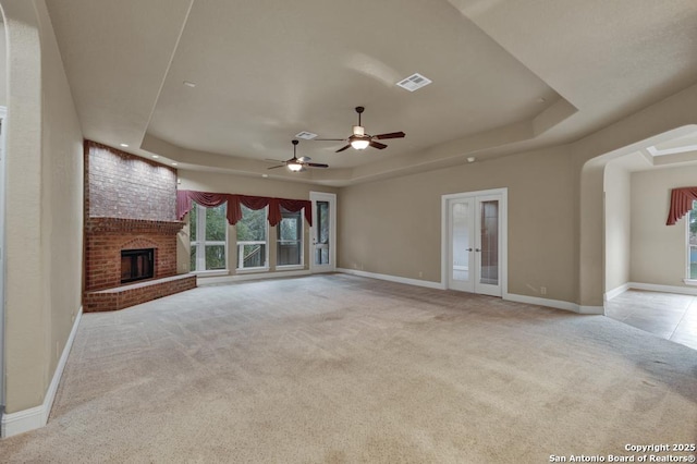 unfurnished living room featuring a fireplace, light colored carpet, ceiling fan, a tray ceiling, and french doors