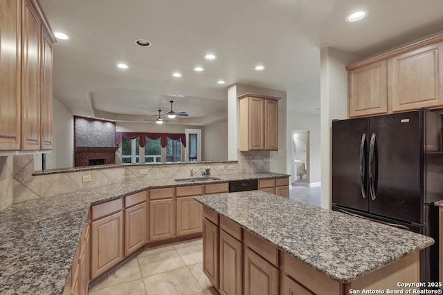 kitchen with light tile patterned floors, sink, black appliances, light stone countertops, and a kitchen island