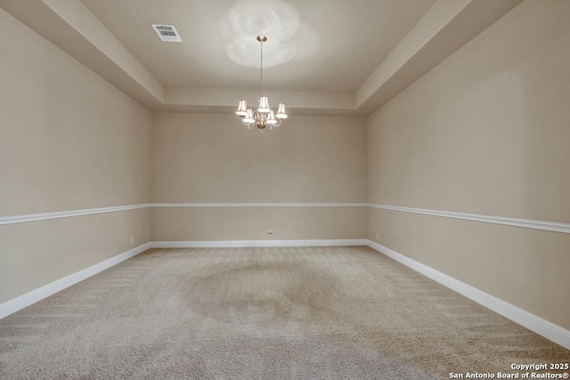 carpeted spare room featuring a raised ceiling and an inviting chandelier