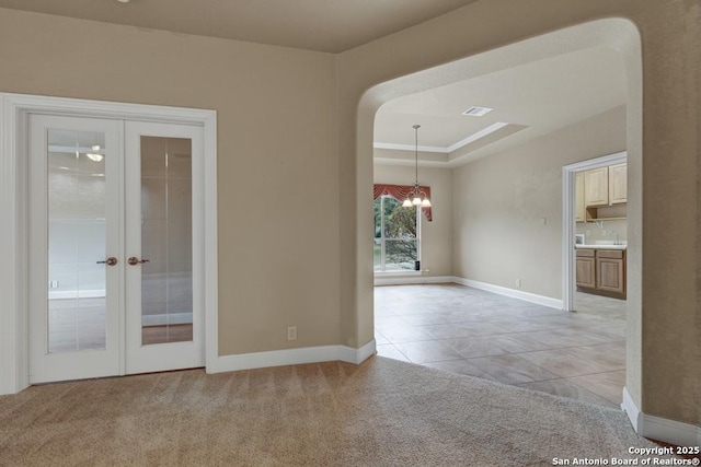 tiled spare room with a tray ceiling, french doors, and a chandelier