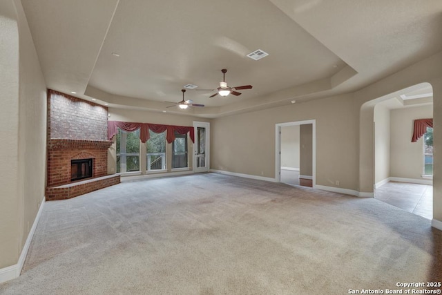 unfurnished living room with a raised ceiling, a brick fireplace, light carpet, and ceiling fan