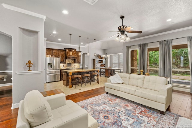 living room with ornamental molding, light wood-type flooring, ceiling fan with notable chandelier, and a textured ceiling