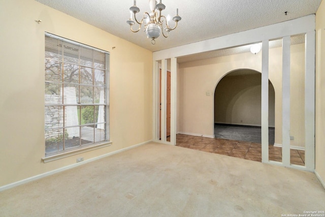 carpeted empty room featuring a notable chandelier and a textured ceiling