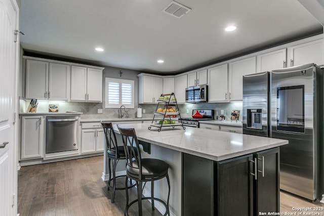 kitchen featuring sink, hardwood / wood-style flooring, appliances with stainless steel finishes, a center island, and light stone counters