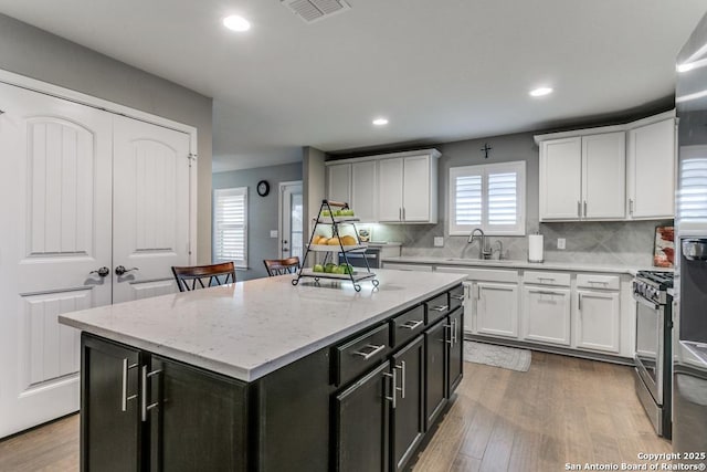 kitchen with sink, stainless steel gas range oven, tasteful backsplash, a kitchen island, and white cabinets