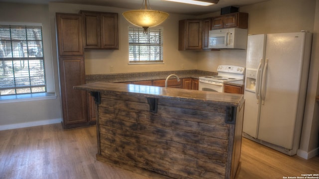 kitchen featuring decorative light fixtures, an island with sink, sink, white appliances, and light wood-type flooring