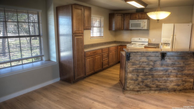 kitchen with white appliances, decorative light fixtures, a kitchen breakfast bar, and light wood-type flooring