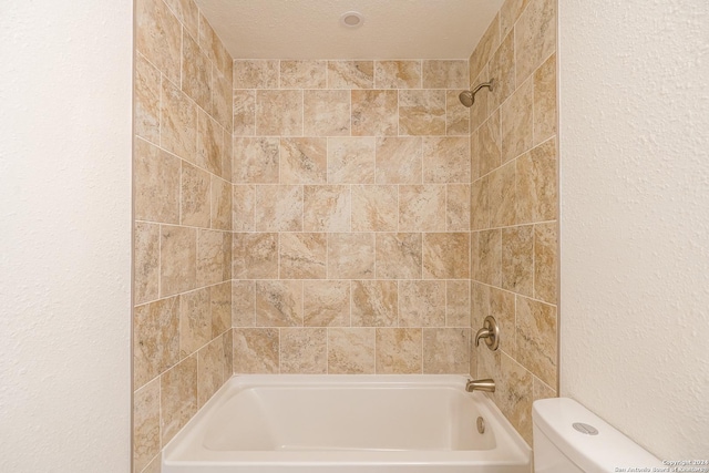 bathroom featuring tiled shower / bath, a textured ceiling, and toilet