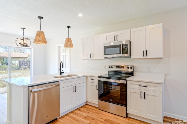 kitchen with appliances with stainless steel finishes, sink, hanging light fixtures, and white cabinets