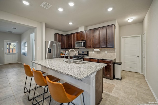 kitchen featuring appliances with stainless steel finishes, an island with sink, sink, a kitchen bar, and light stone counters