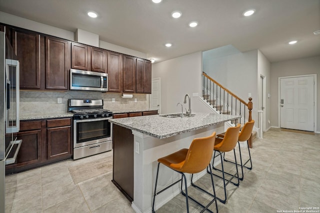 kitchen featuring sink, appliances with stainless steel finishes, an island with sink, light stone countertops, and backsplash