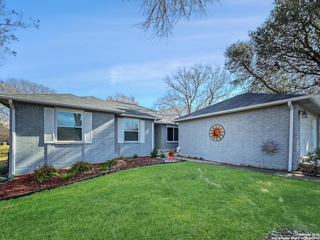 ranch-style house featuring an outbuilding, brick siding, an attached garage, and a front lawn