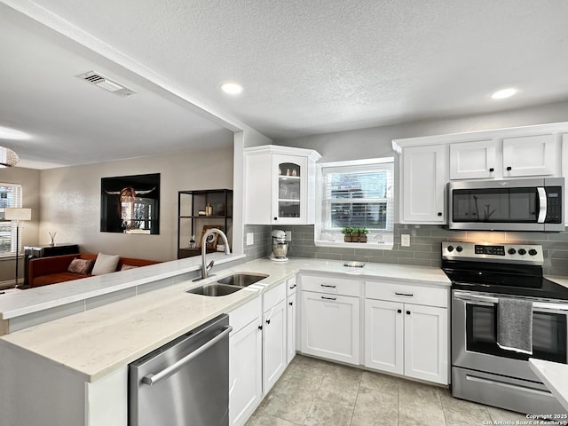 kitchen with stainless steel appliances, tasteful backsplash, visible vents, a sink, and a peninsula