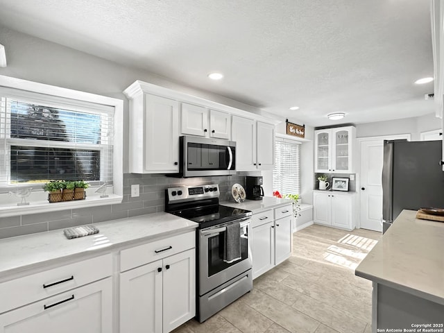 kitchen with appliances with stainless steel finishes, plenty of natural light, white cabinets, and decorative backsplash