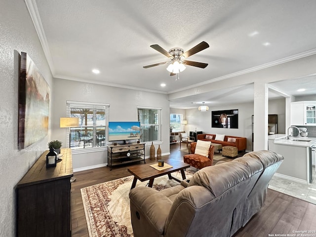 living area featuring a textured ceiling, wood finished floors, a ceiling fan, baseboards, and ornamental molding