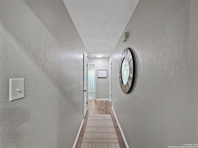 hall with a textured ceiling, baseboards, wood finished floors, and a textured wall