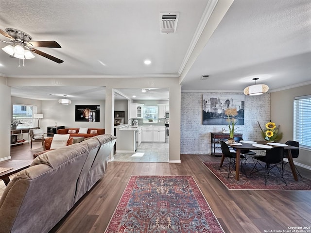 living area with visible vents, ornamental molding, a textured ceiling, brick wall, and wood finished floors