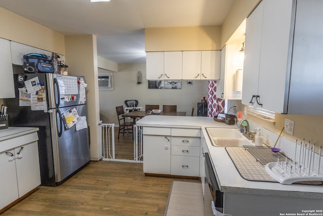 kitchen featuring sink, wood-type flooring, stainless steel refrigerator, kitchen peninsula, and white cabinets