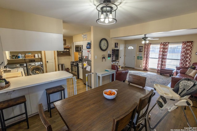 dining room with sink, ceiling fan with notable chandelier, washer and clothes dryer, and light wood-type flooring