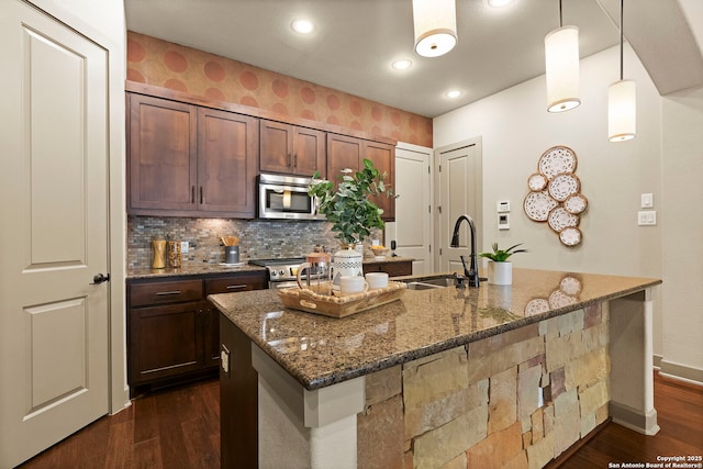 kitchen featuring appliances with stainless steel finishes, decorative light fixtures, sink, dark stone countertops, and backsplash