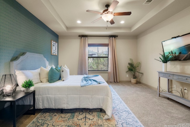 carpeted bedroom with ceiling fan and a raised ceiling