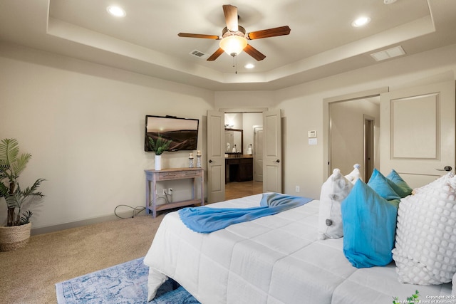 bedroom with ensuite bath, a raised ceiling, and ceiling fan