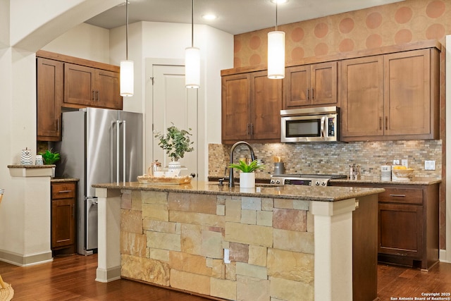 kitchen featuring appliances with stainless steel finishes, an island with sink, sink, backsplash, and dark stone counters