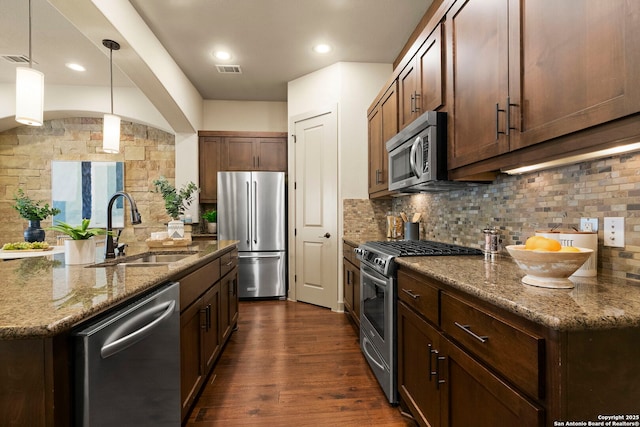 kitchen with sink, appliances with stainless steel finishes, decorative backsplash, decorative light fixtures, and dark stone counters