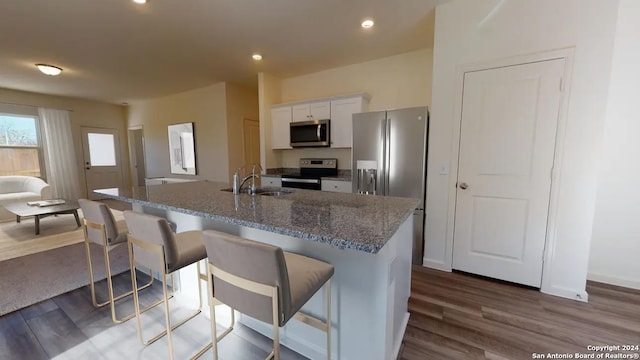 kitchen featuring appliances with stainless steel finishes, sink, white cabinets, a kitchen bar, and dark stone counters