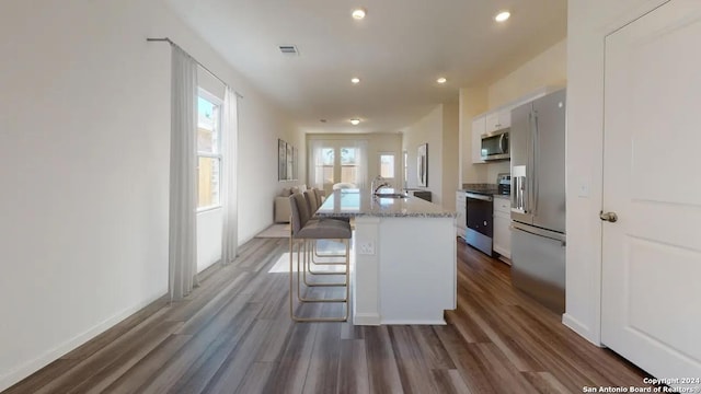 kitchen featuring dark wood-type flooring, appliances with stainless steel finishes, a kitchen breakfast bar, an island with sink, and white cabinets