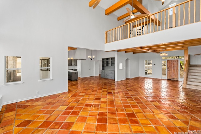 unfurnished living room featuring beam ceiling, ceiling fan with notable chandelier, and a high ceiling