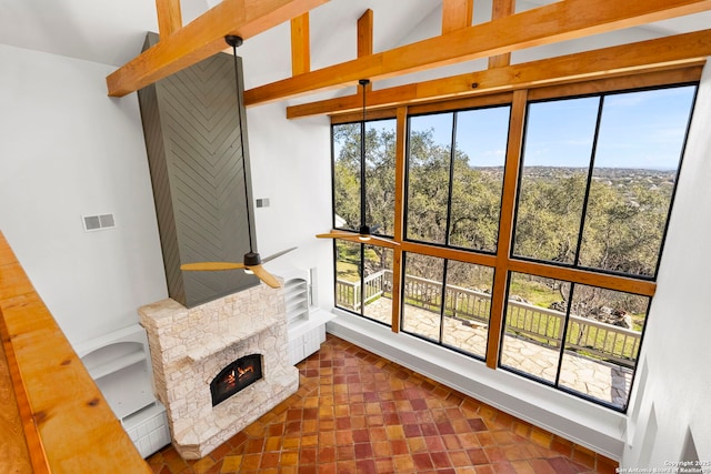 interior space featuring beam ceiling, a stone fireplace, high vaulted ceiling, and ceiling fan