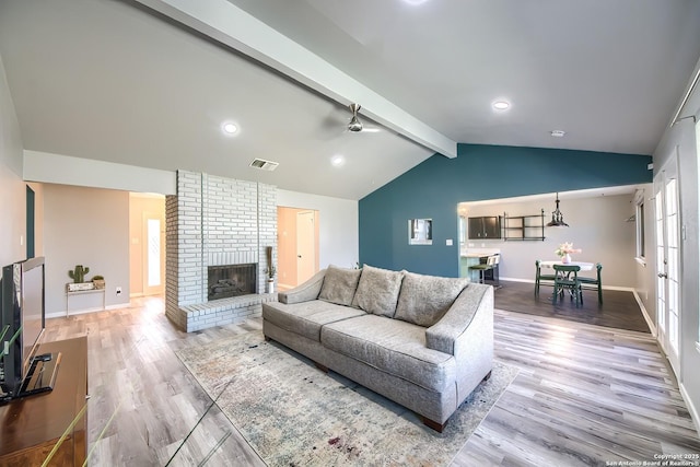 living room with hardwood / wood-style flooring, ceiling fan, vaulted ceiling with beams, and a fireplace